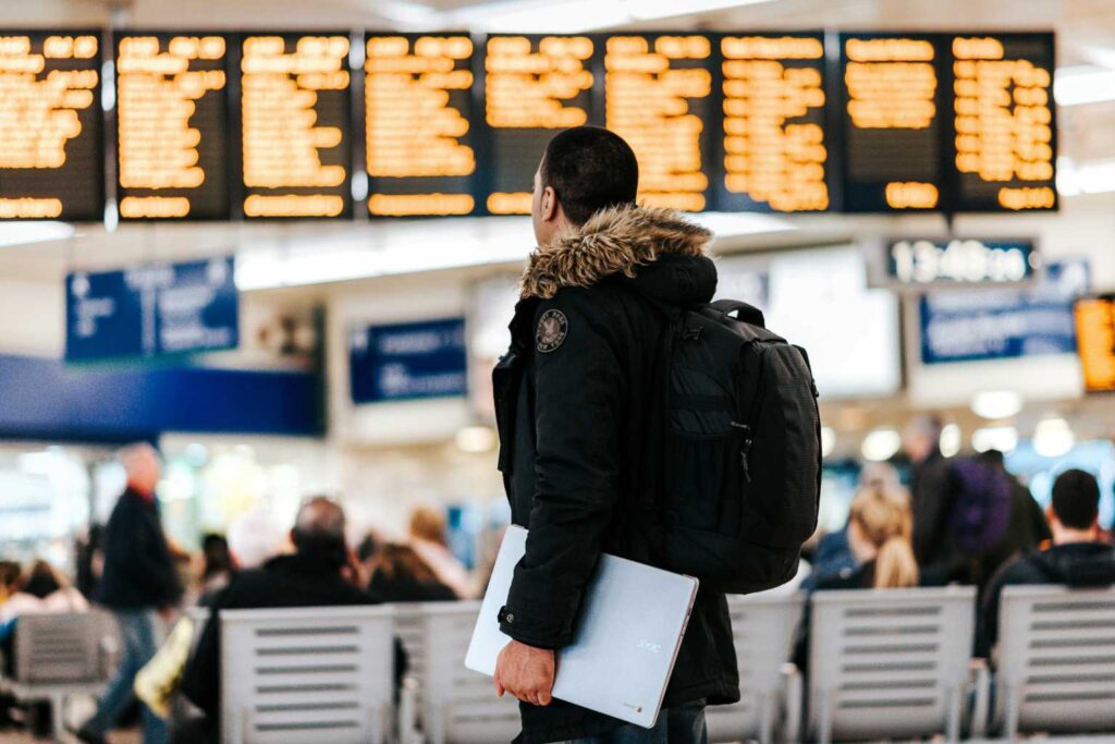 Foto von Anete Lūsiņa auf Unsplash - Mann steht im Flughafen und schaut auf LED-Flugplanpinnwand